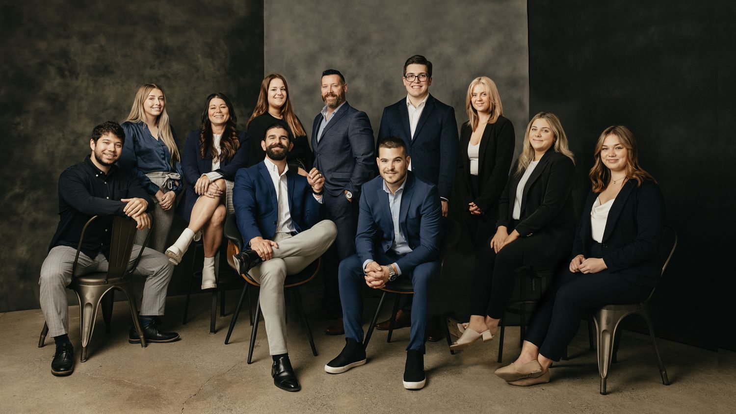 Business team photo shoot with professionals in formal attire seated against dark background.