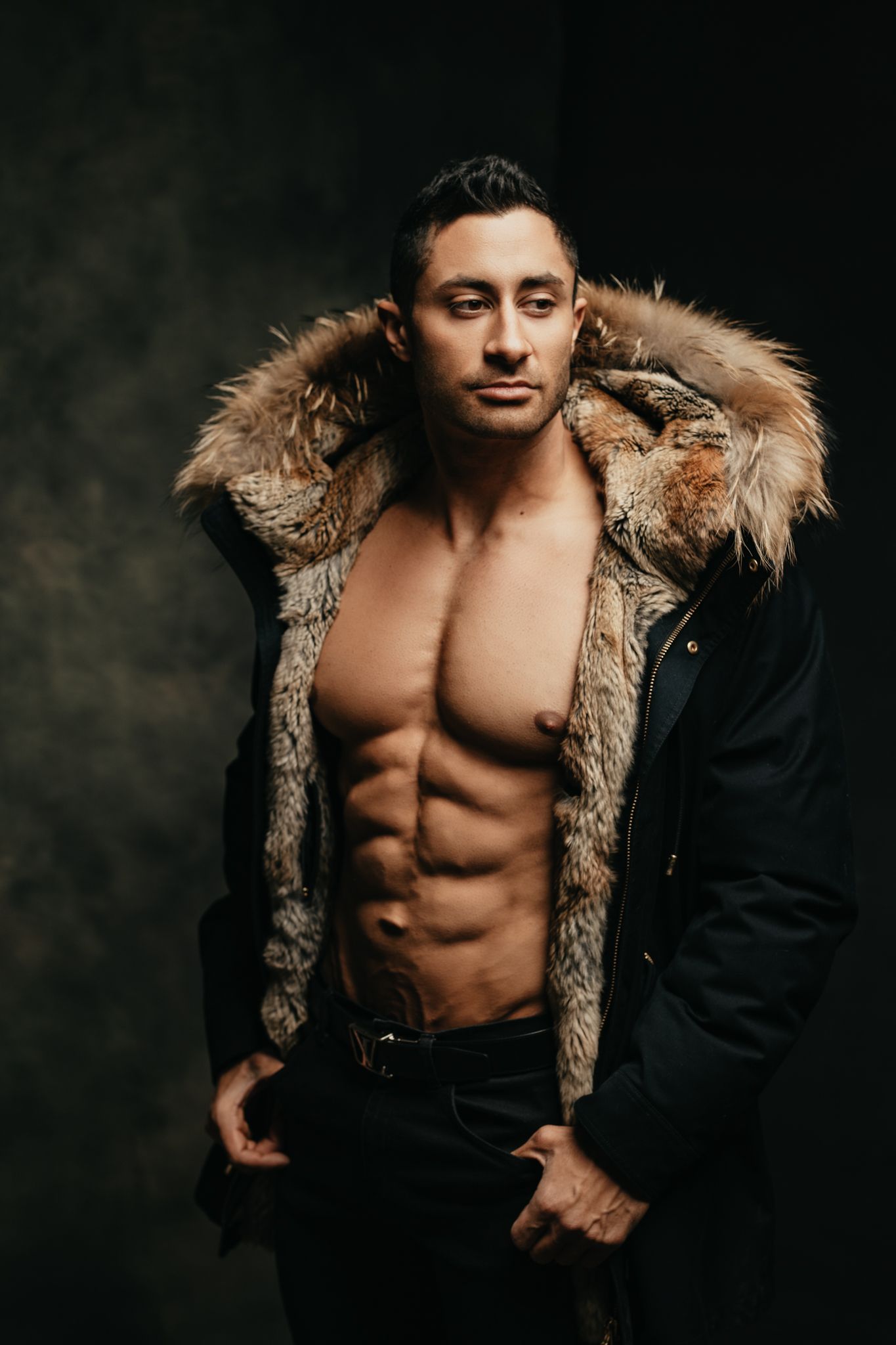 Fashion portrait featuring fur-trimmed jacket against dark studio background.