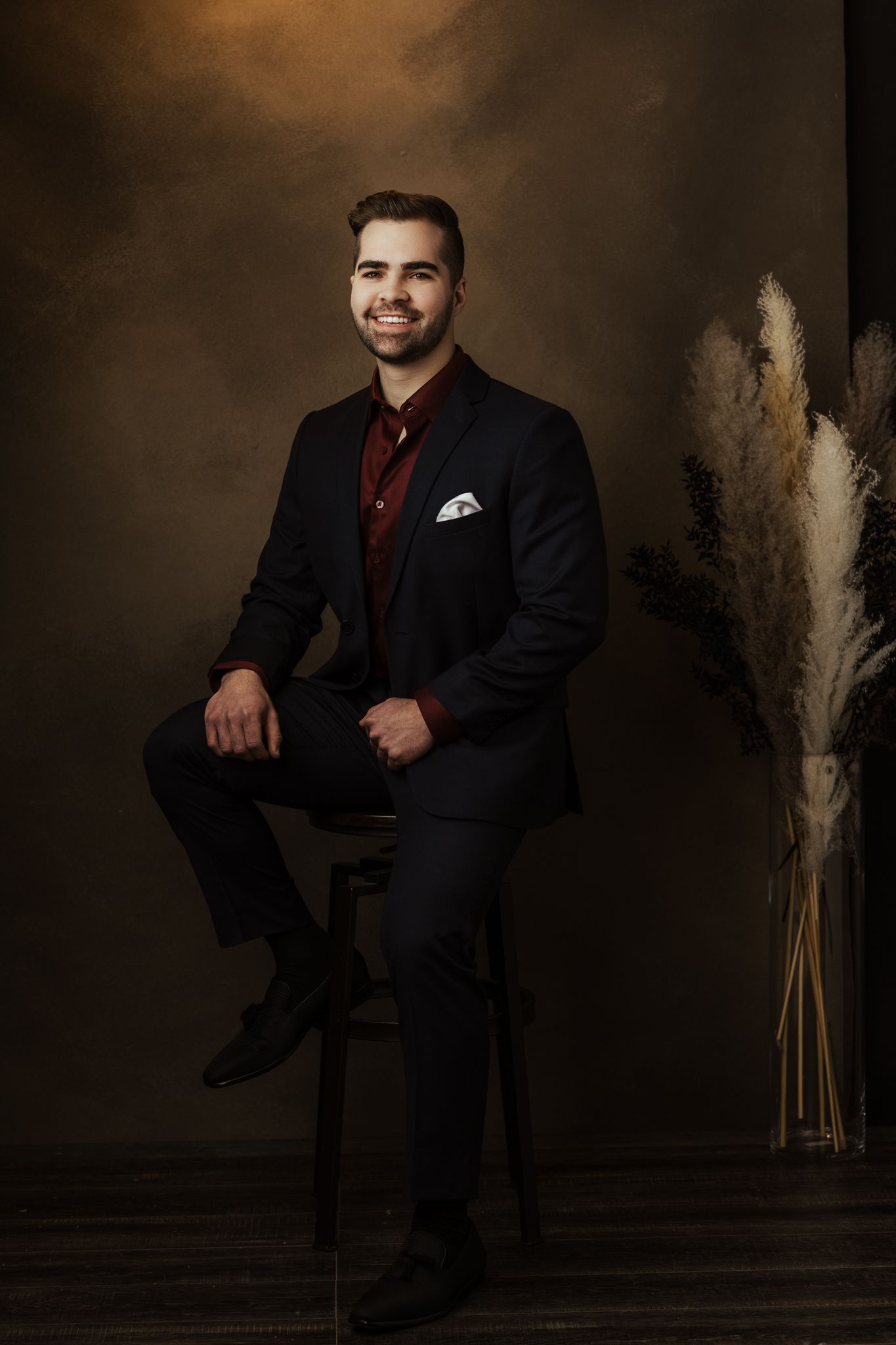 Formal portrait series in black suit and burgundy tie against moody studio backdrop.