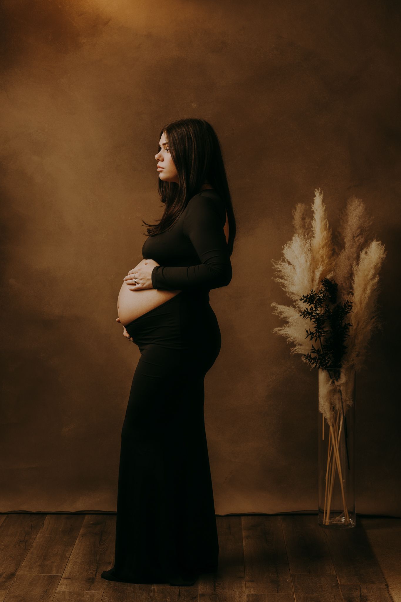 Elegant maternity portrait with dried pampas grass decor in a warm sepia tone setting.