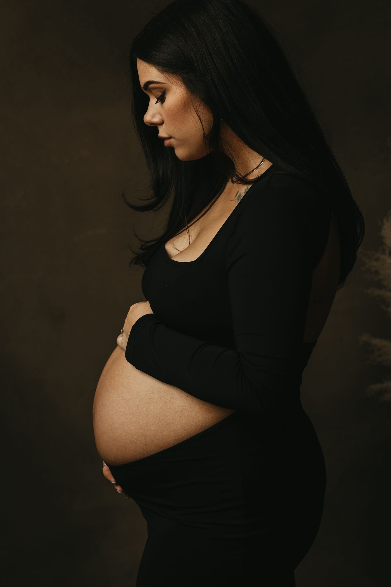 Artistic maternity photoshoot featuring a silhouette in black against a dark moody background.