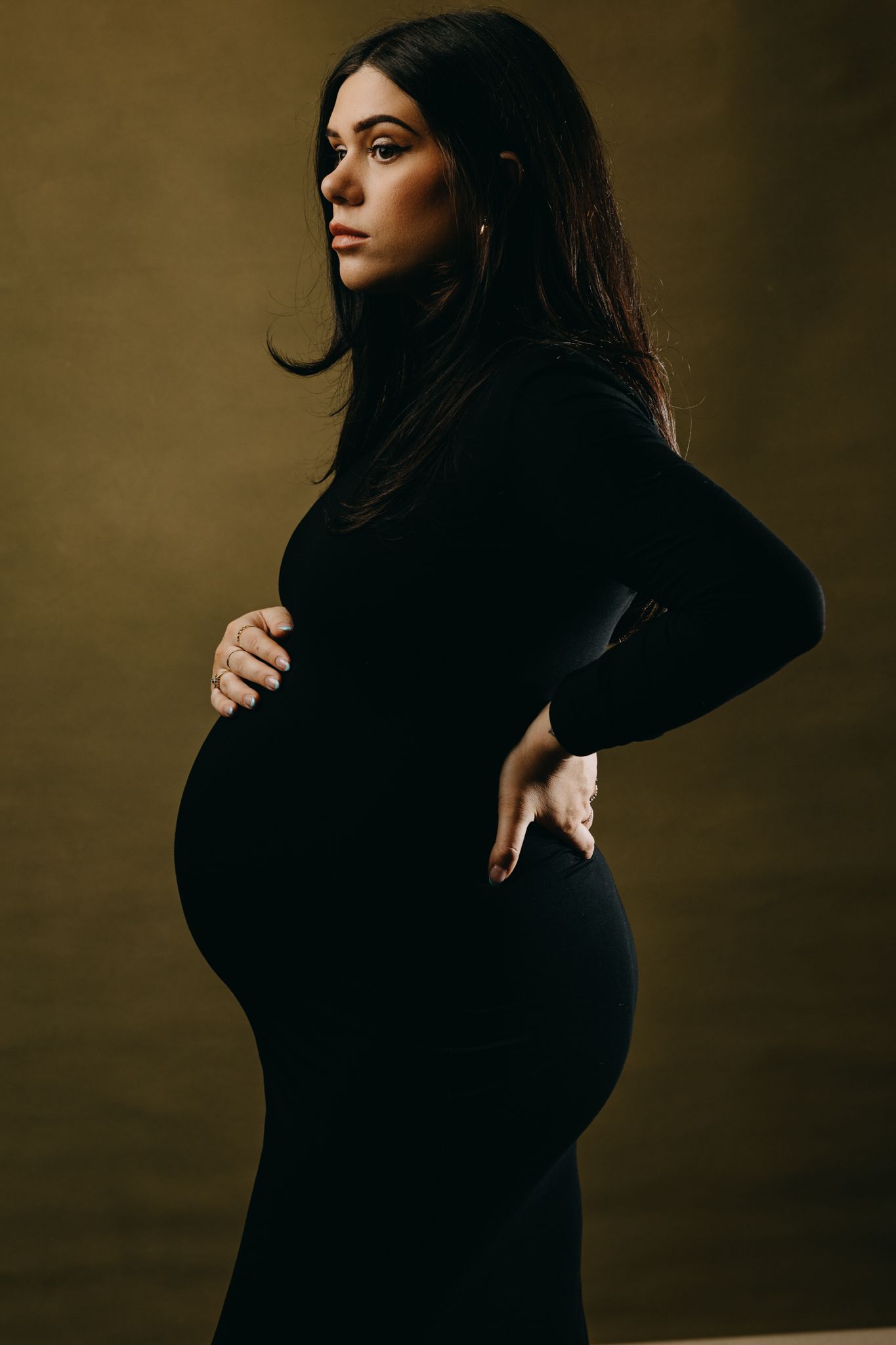 Dramatic black and white maternity photos showing profile poses in dark clothing.