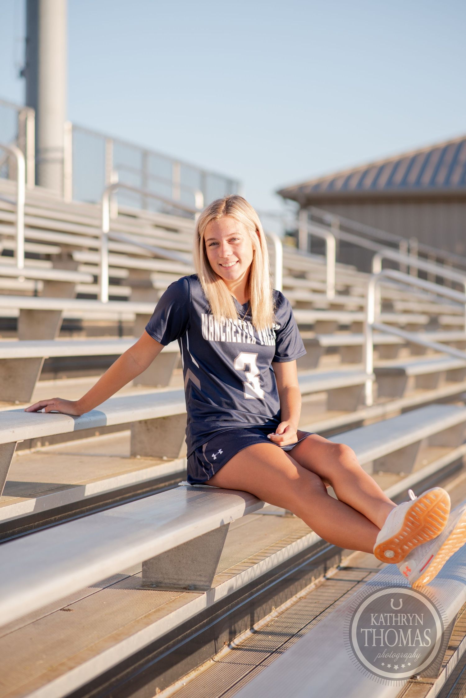 Athletic portrait on metal bleachers wearing a navy sports uniform and orange shoes.