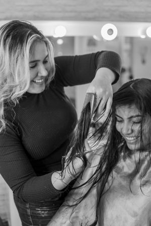 Hairstylist in black sweater styling client's hair in salon with bright lighting.
