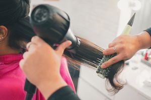 Close-up of hairdresser using blow dryer and brush on client's dark hair.