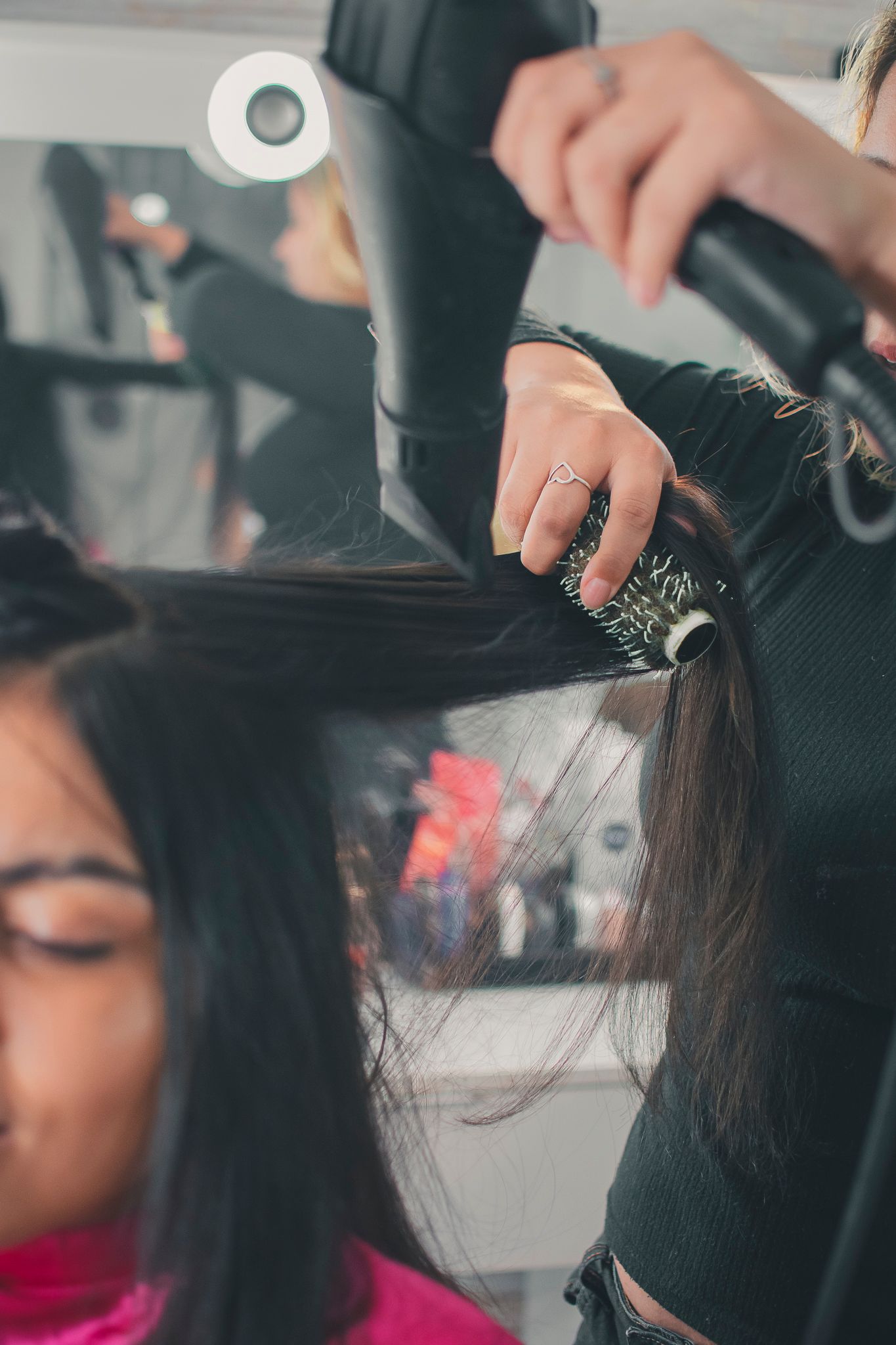 Hair stylist working on styling dark hair with professional tools and equipment in salon setting.