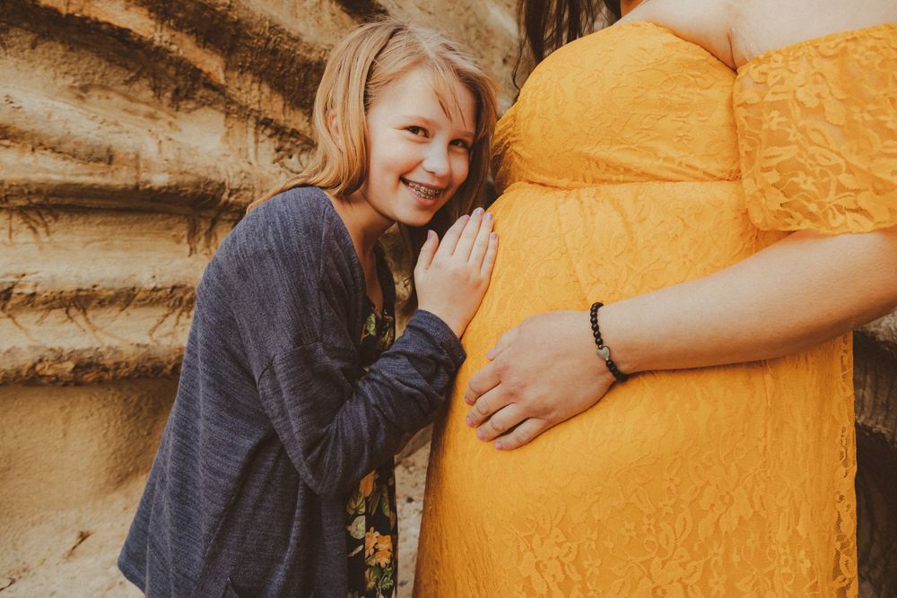Joyful moment captured during maternity shoot with yellow dress against rocky backdrop.