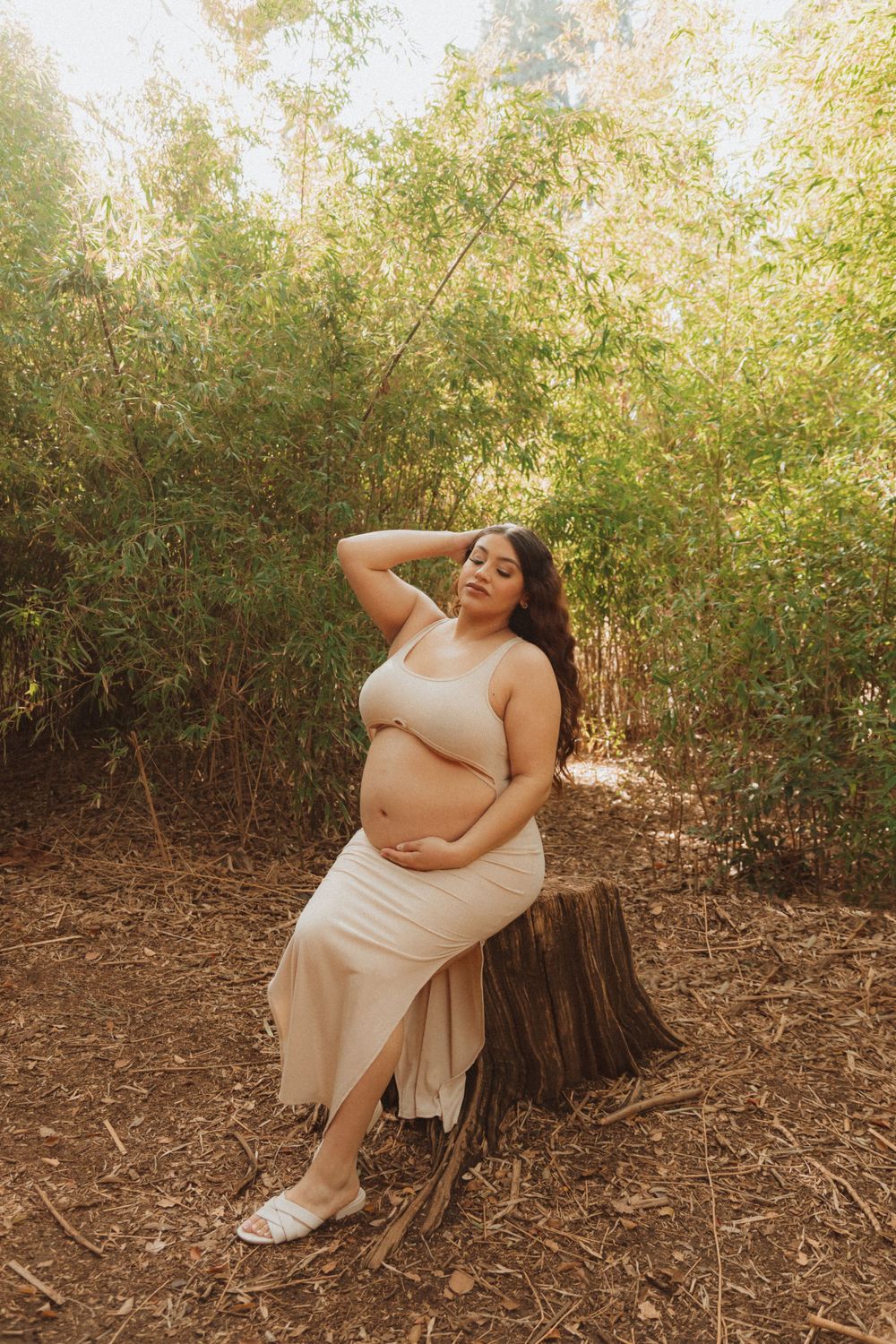 A joyful maternity moment captured in a natural forest setting with warm lighting.