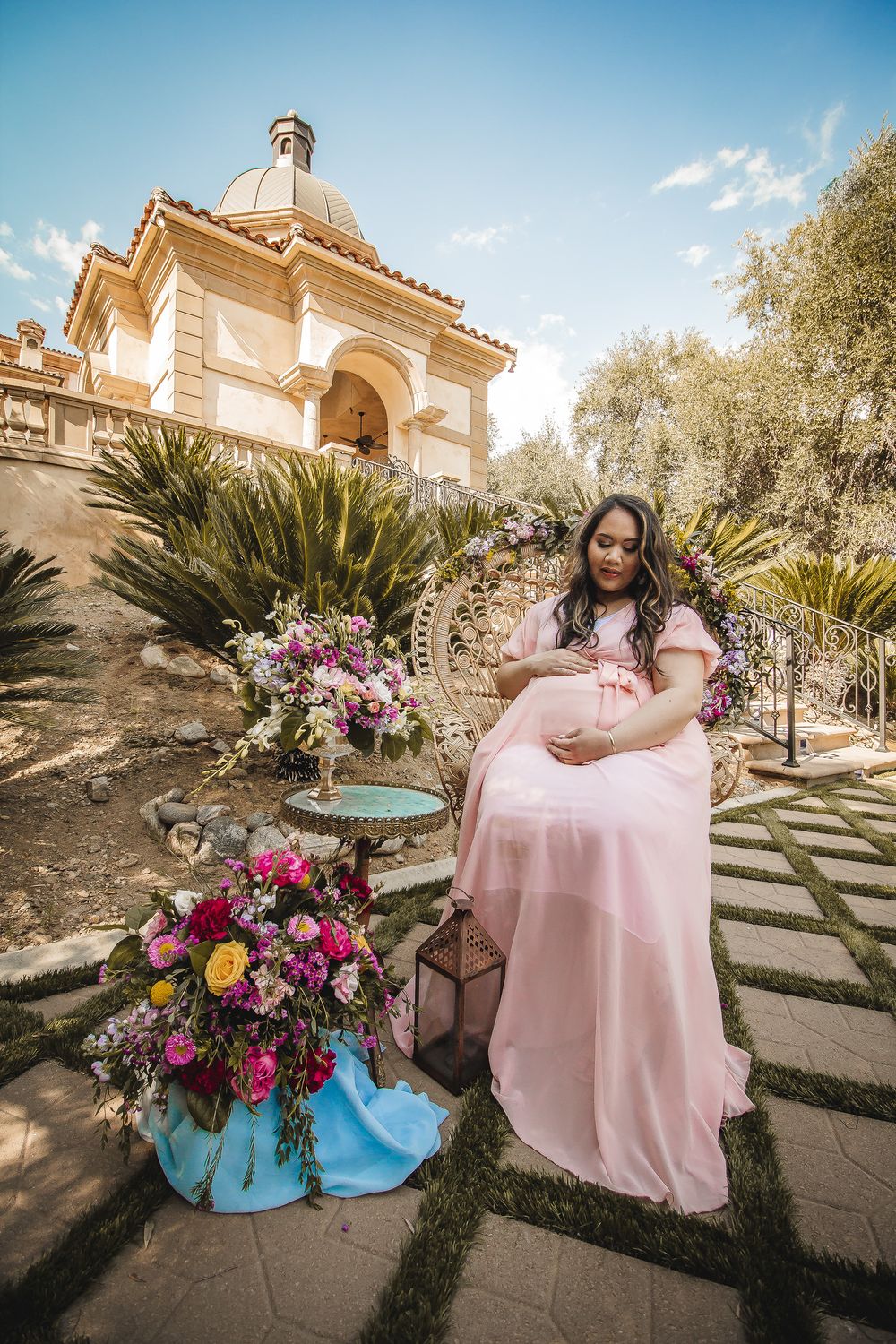 Elegant outdoor maternity portrait with pink dress and vibrant floral arrangements near a domed structure.