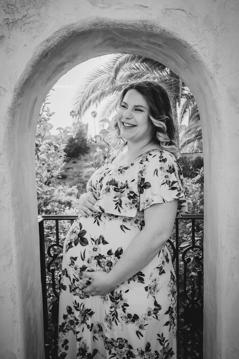 Black and white maternity portrait showcasing joy through an arched doorway with palm trees.