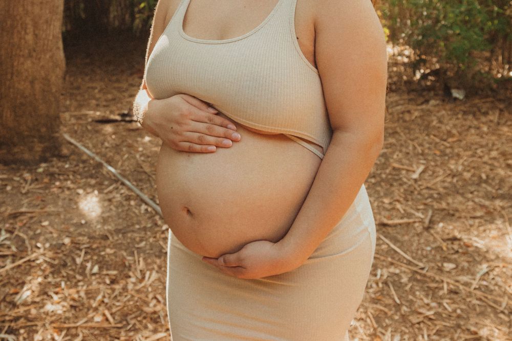 A close-up maternity photo showing hands cradling a baby bump in cream-colored clothing.
