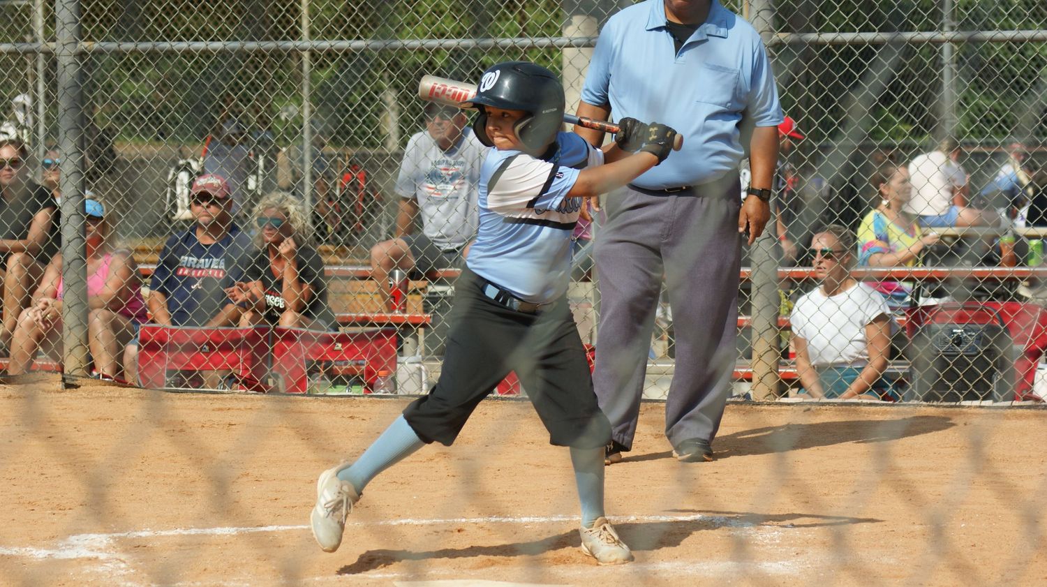 A softball player in mid-swing stance at home plate during a game with spectators watching.