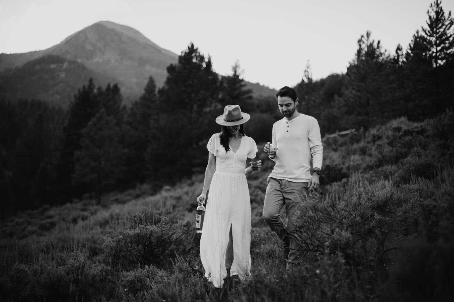 A black and white photo of a couple walking together on a mountain trail with scenic views.