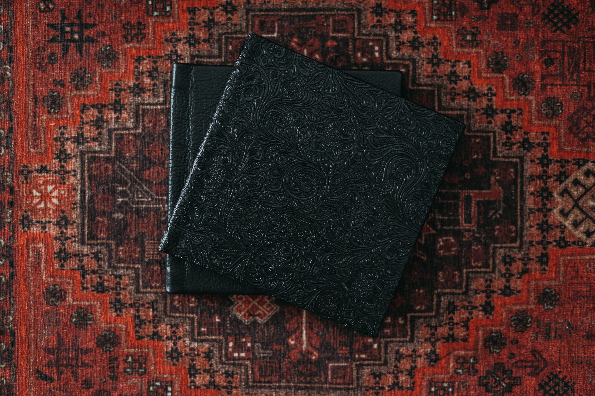 Stack of black leather albums arranged on red oriental carpet.