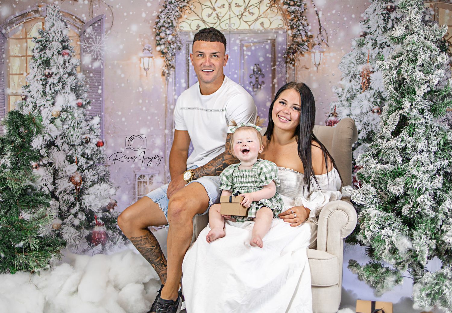 Young family poses together in a festive Christmas studio portrait with decorated trees.