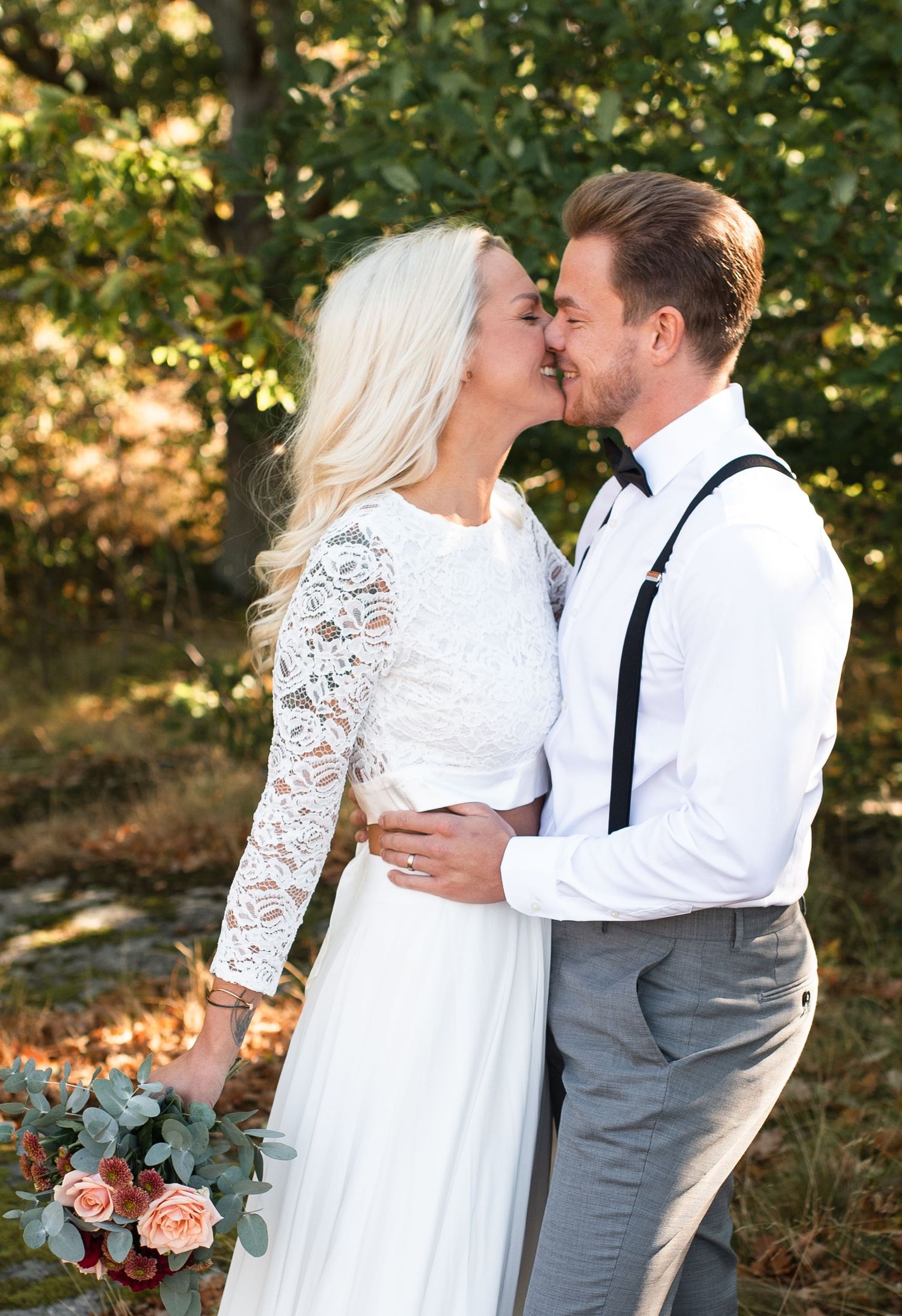 A romantic wedding moment captured in a forest setting with warm golden sunlight filtering through the trees.