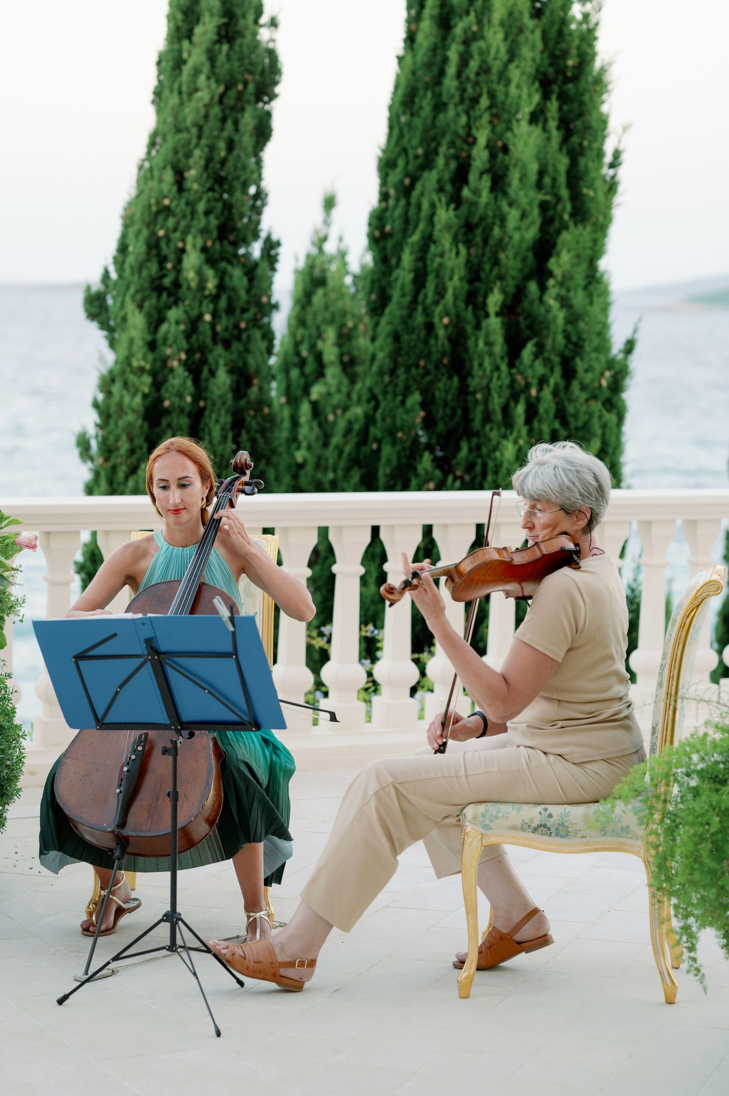 Musicians perform with cello and violin on an elegant terrace overlooking the sea.