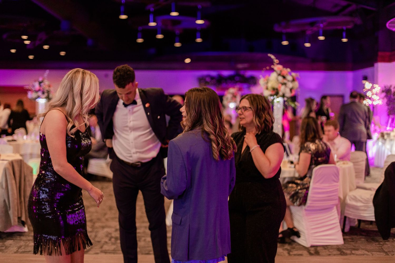 Wedding guests socializing on the dance floor at a reception with purple ambient lighting.