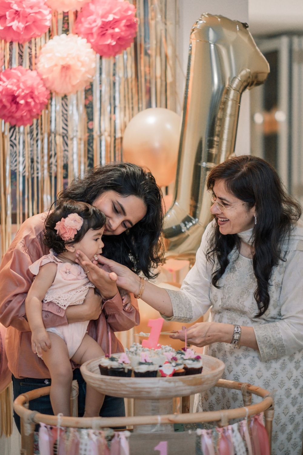 Joyful gathering around a baby at a festive party decorated with pink pom poms and balloons.