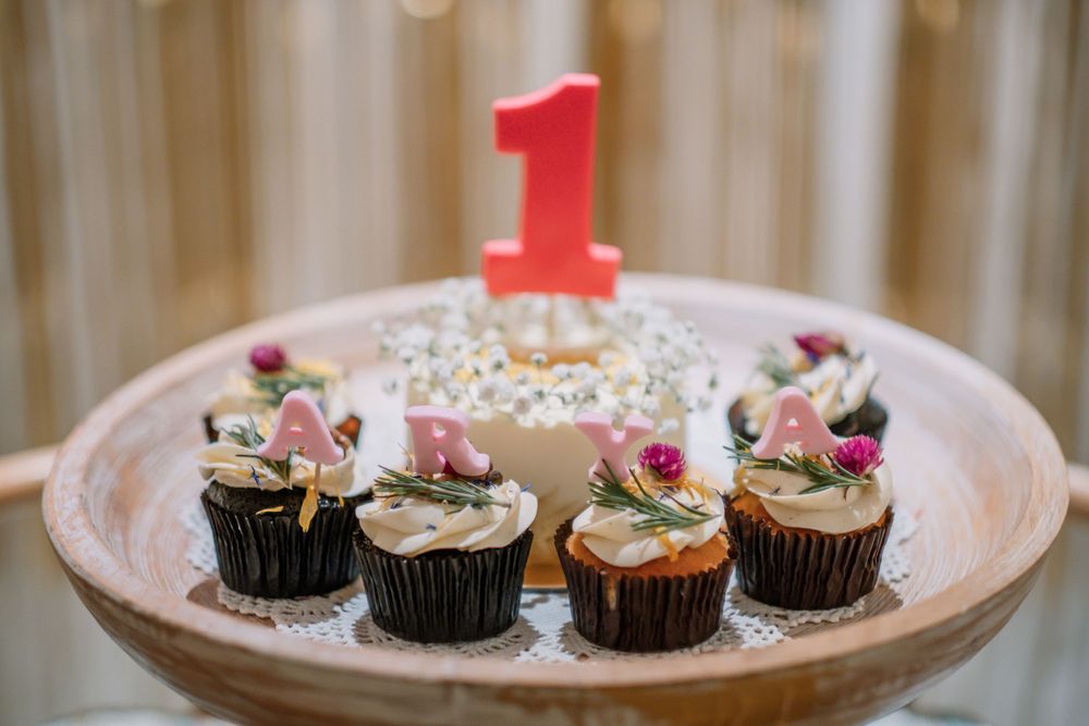 Chocolate cupcakes decorated with pink flowers and a red number one candle on a wooden plate for first birthday.
