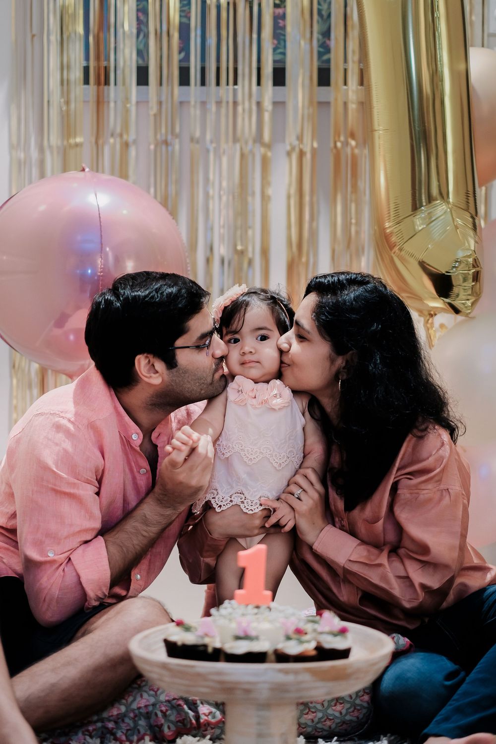 First birthday celebration with pink and gold party decorations and cupcakes on display.