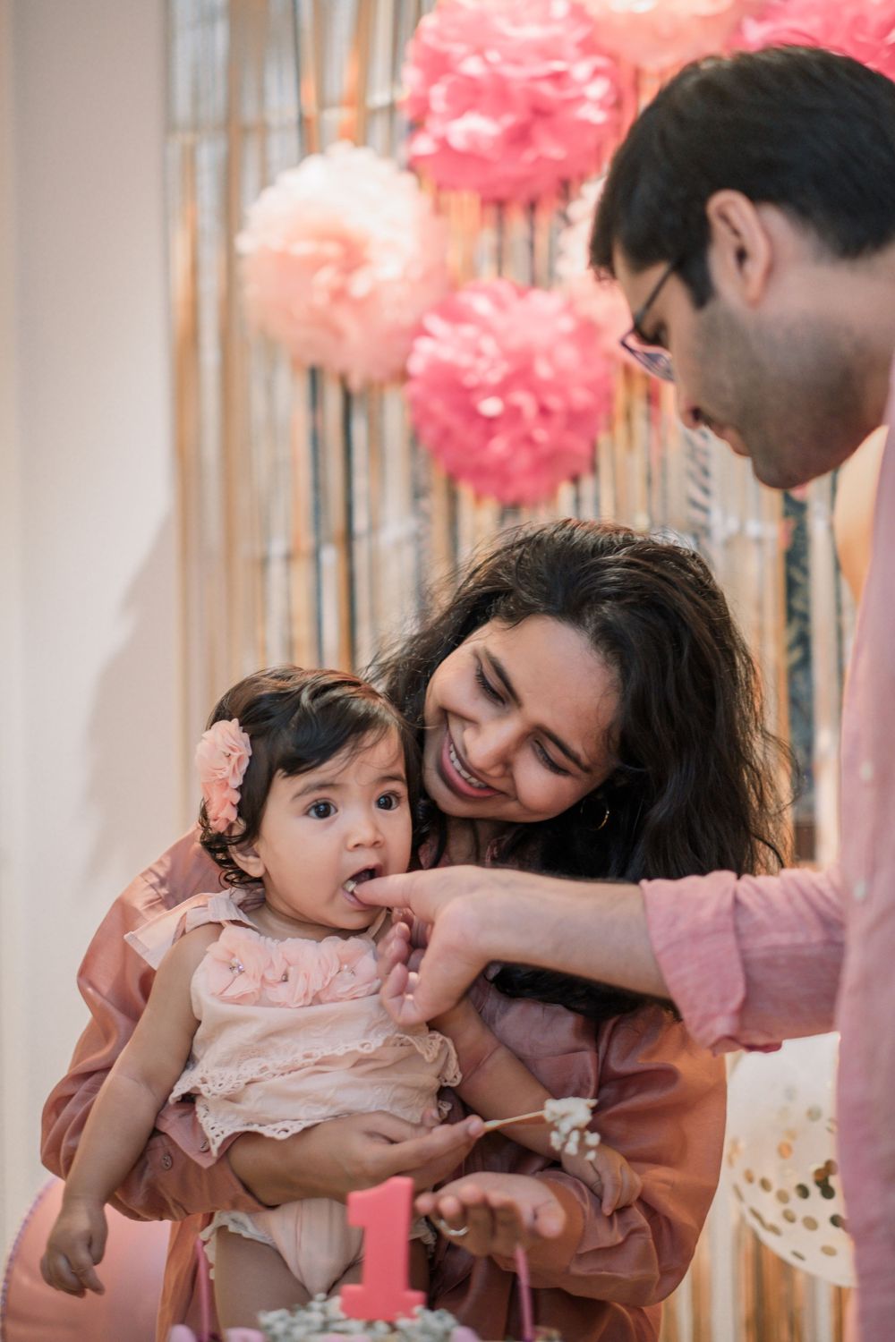 A sweet family moment at a pink-themed party with decorative tissue poms overhead.