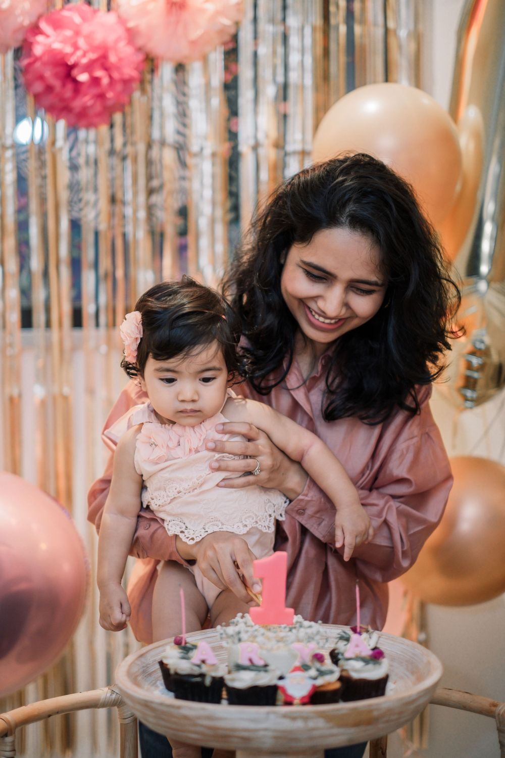 First birthday party scene with pink decorations and cupcakes on display.
