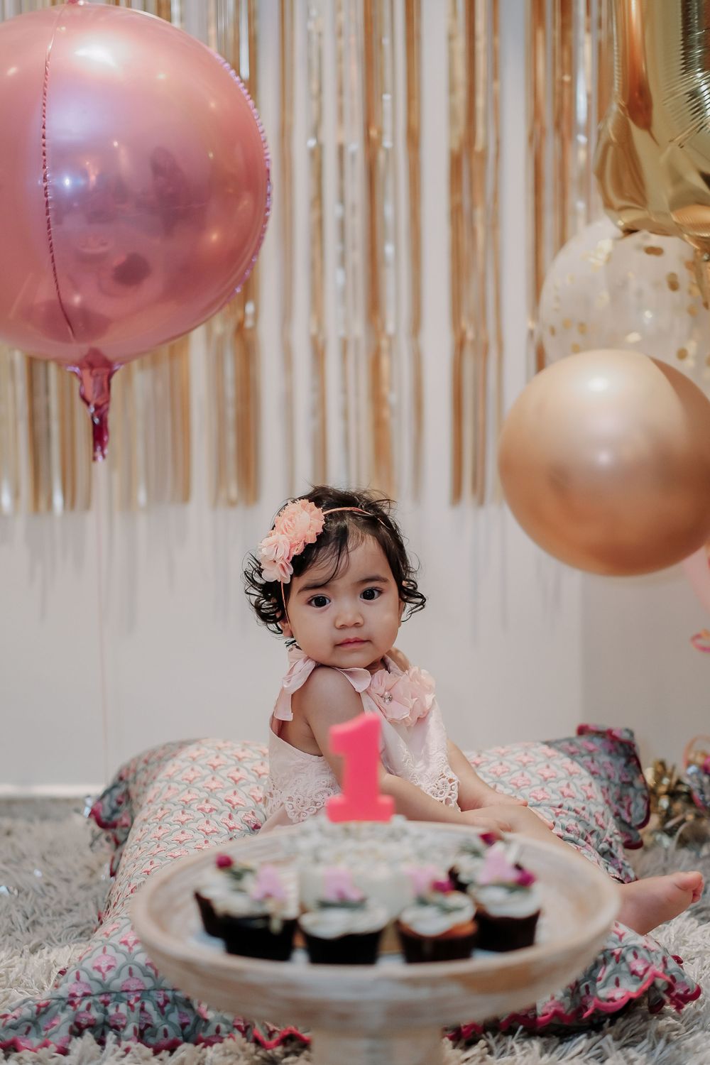 Intimate first birthday celebration with pink balloons, cupcakes, and metallic streamers.
