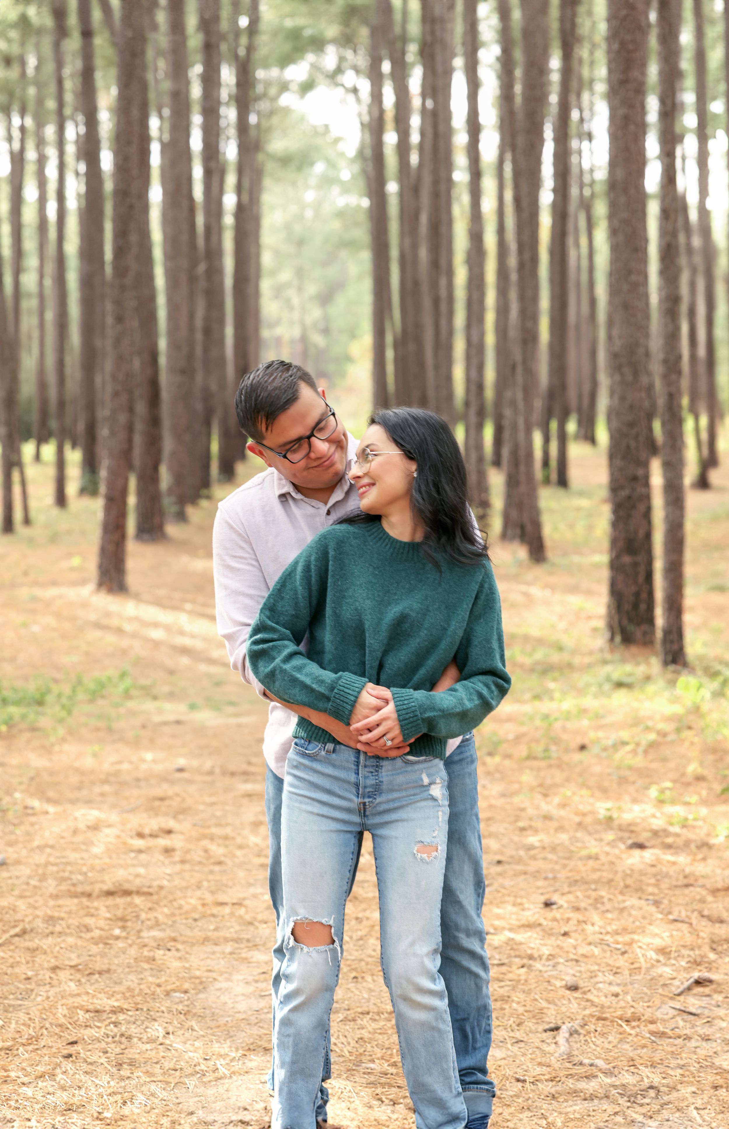 Couple shares intimate moment in pine forest during casual photoshoot.