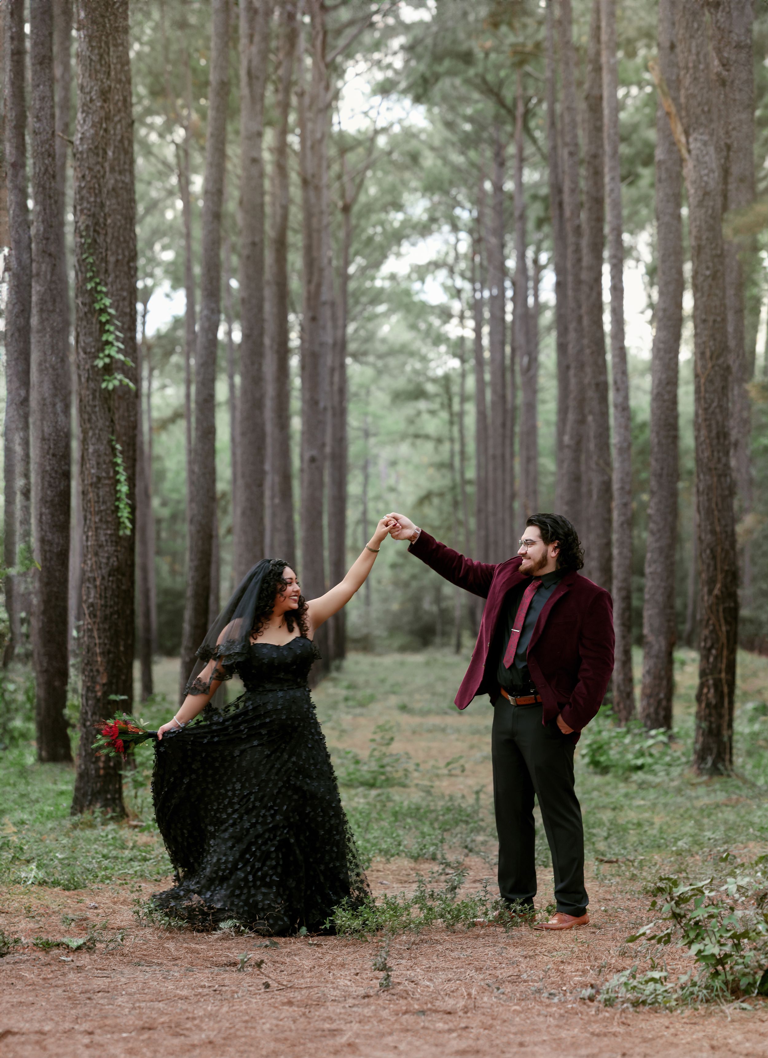 Romantic forest engagement photo of couple dancing among tall pine trees.