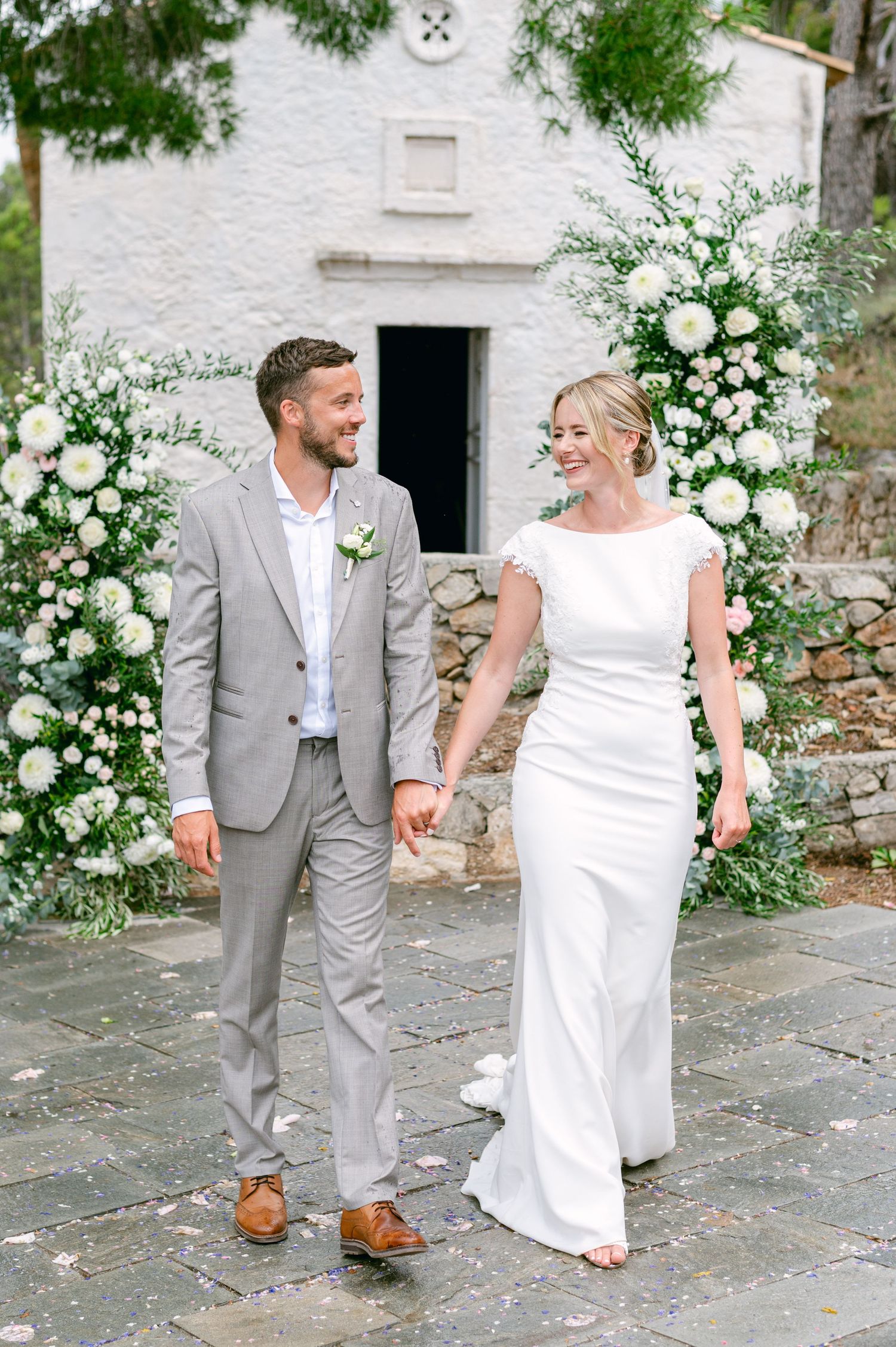 An elegant wedding couple poses in front of a white building adorned with beautiful floral arrangements.