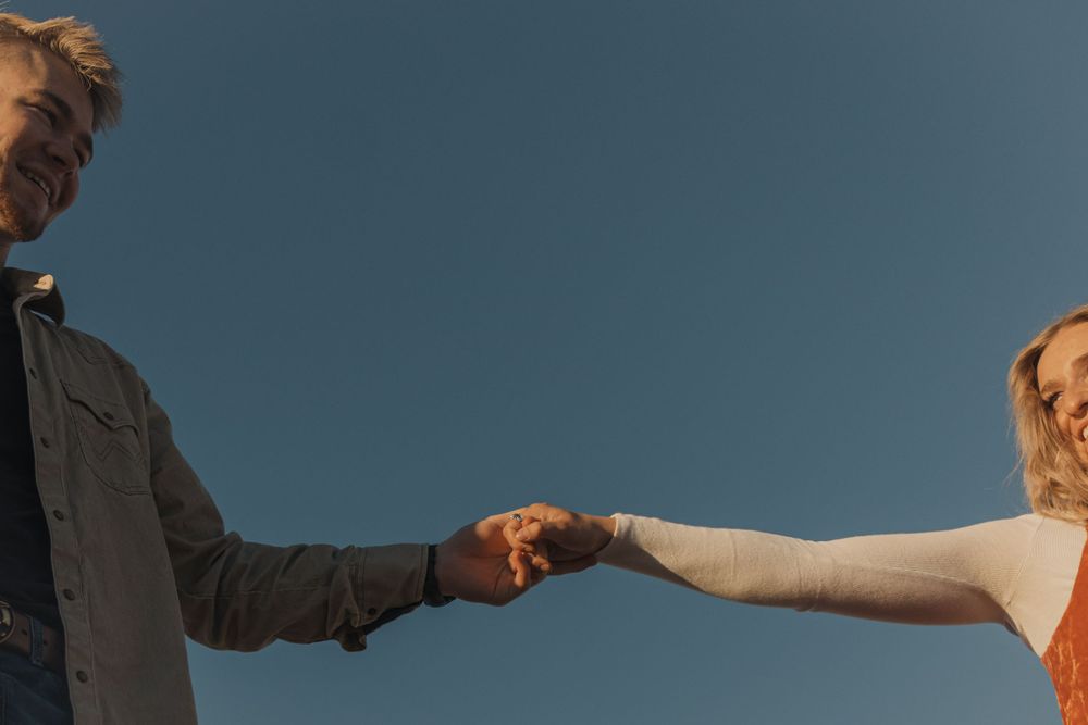 Two people holding hands against a blue sky in an intimate romantic moment.