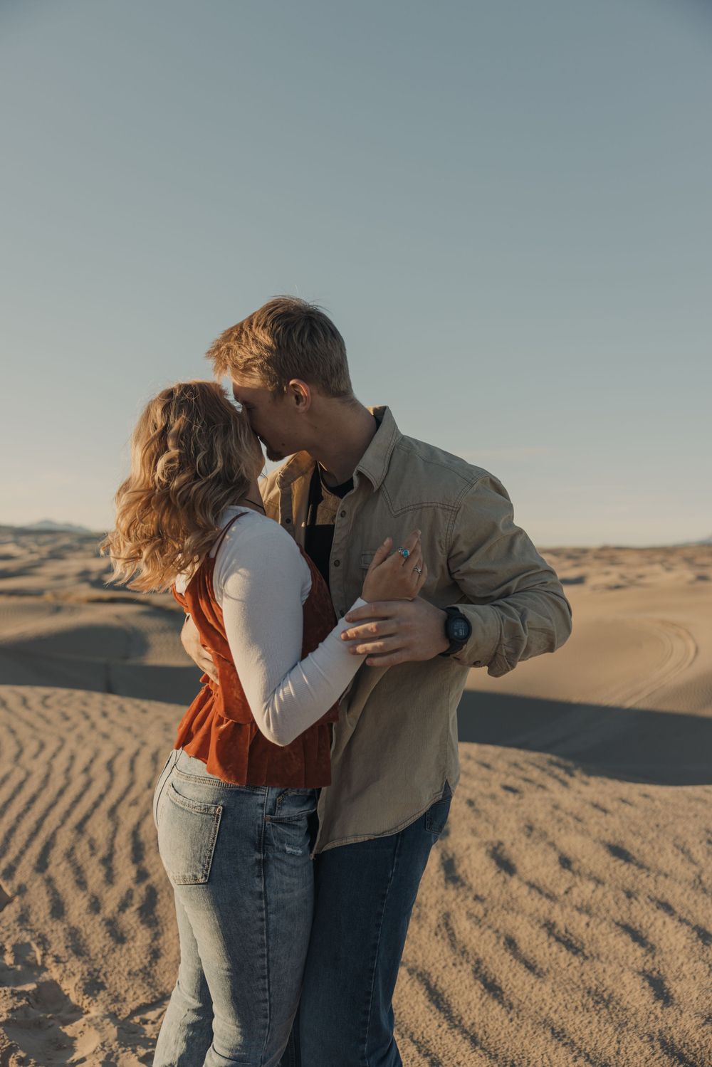 Romantic moment between couple in desert sand dunes during golden hour.