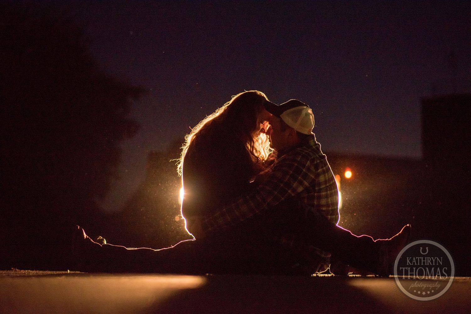 Silhouetted couple sharing intimate moment with dramatic backlit glow at night.