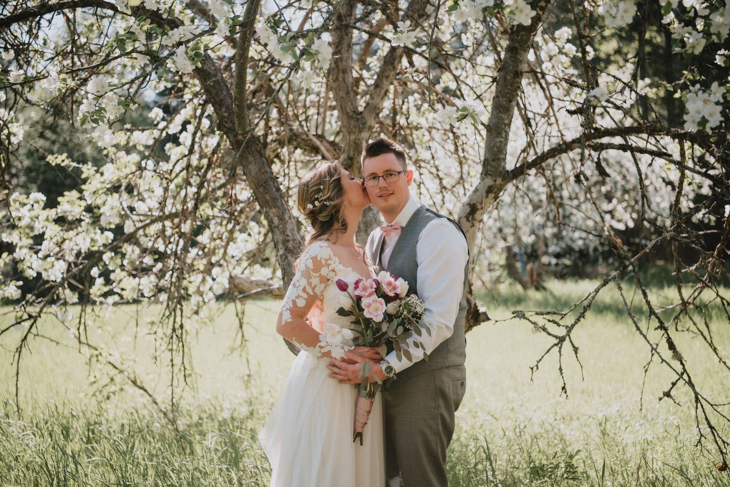 Wedding portrait under blooming spring trees with pink floral bouquet.