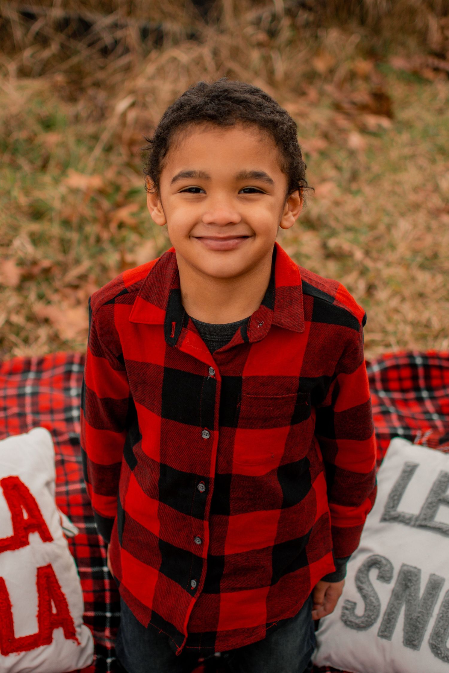 Child wearing red and black buffalo plaid shirt smiling during outdoor photo session.