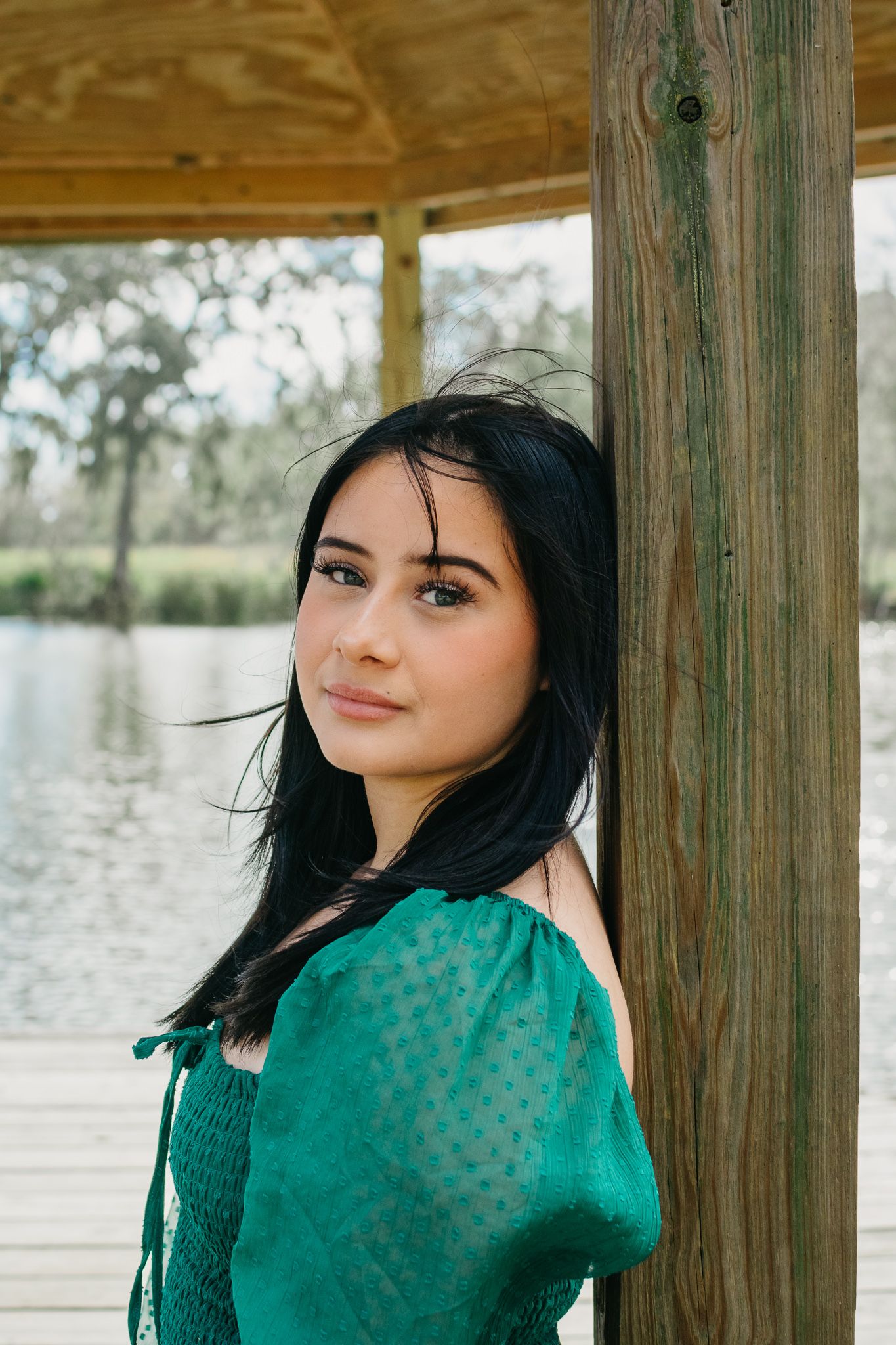 Woman in emerald green dress posing by wooden pier post.