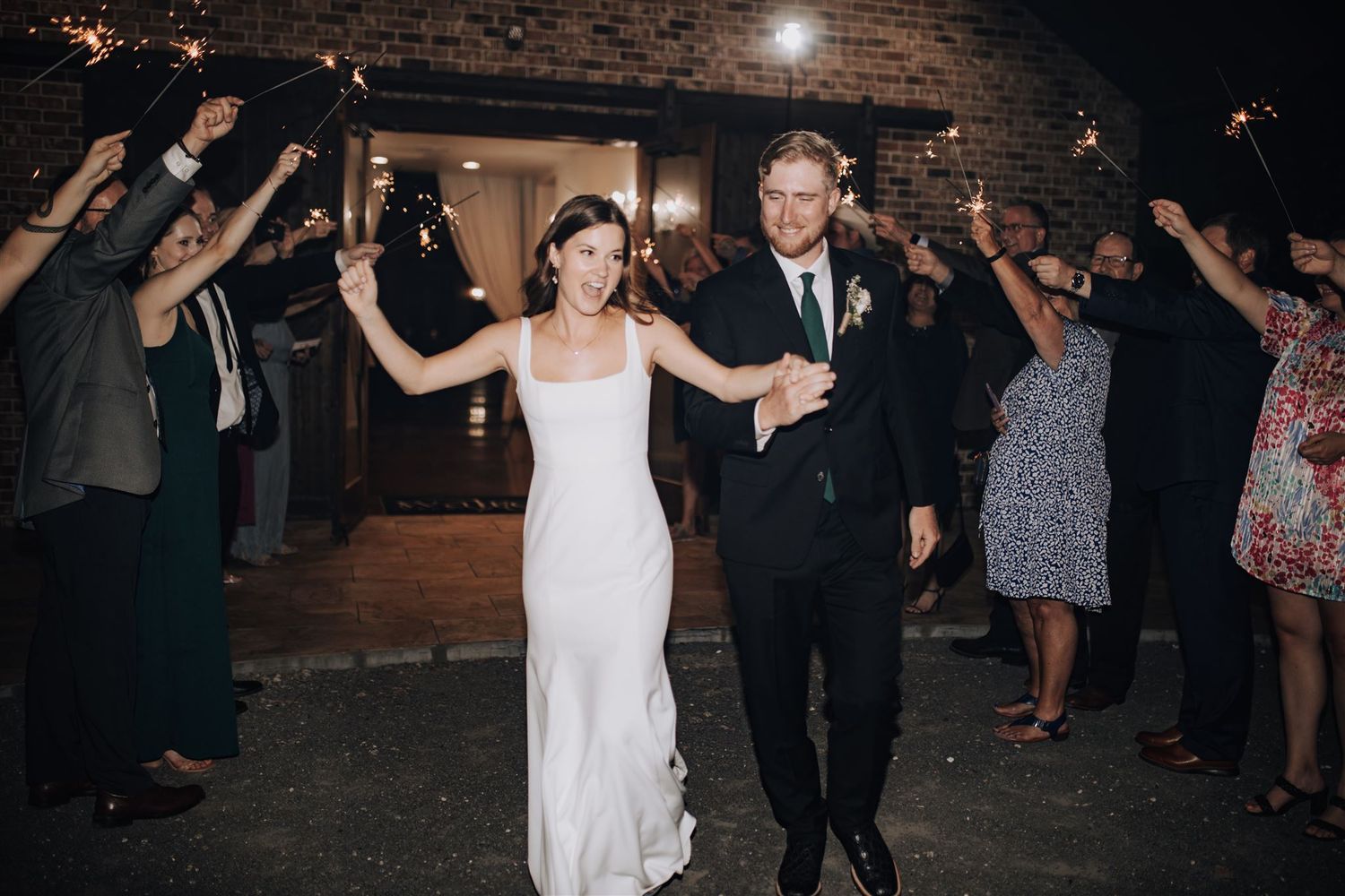 Newlyweds make their exit through cheering guests outside brick venue at night.