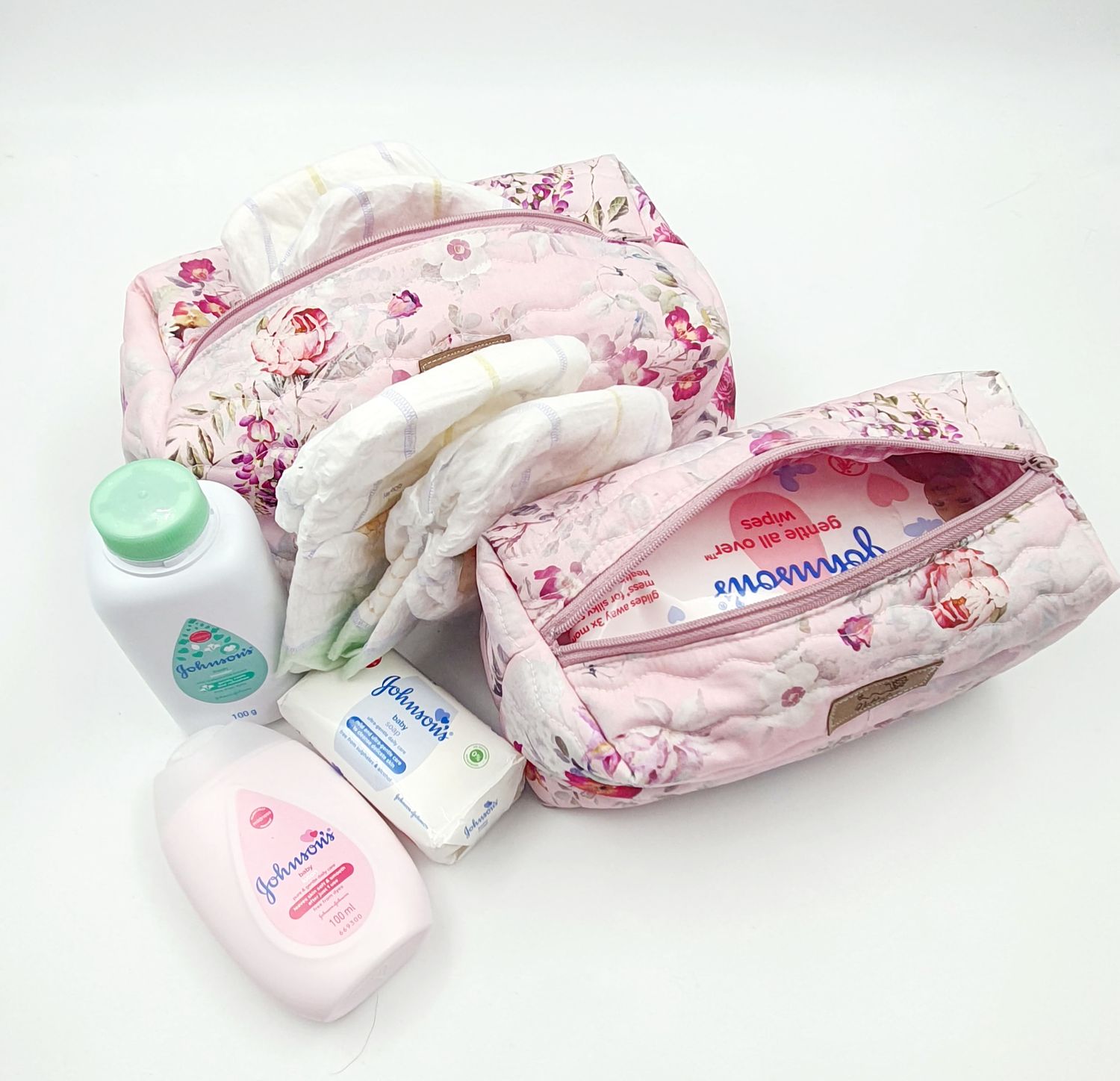Pink floral diaper bags containing baby care essentials and toiletries.
