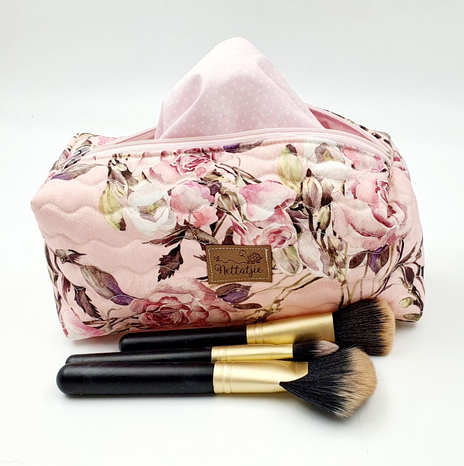 Floral print makeup brush holder case with gold-trimmed brushes displayed in various positions.
