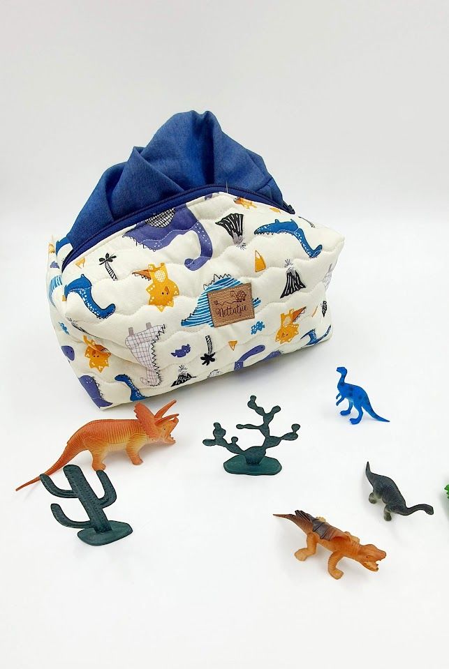 Blue and white dinosaur print toy storage bag with plastic dinosaur figures scattered around.