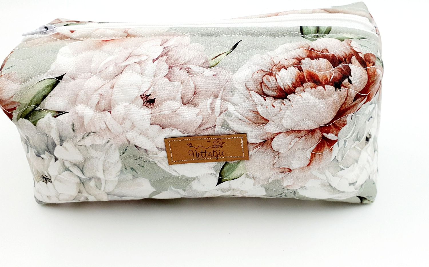 Elegant toiletry bag featuring large peony floral print in pink and white with leather accent tag.