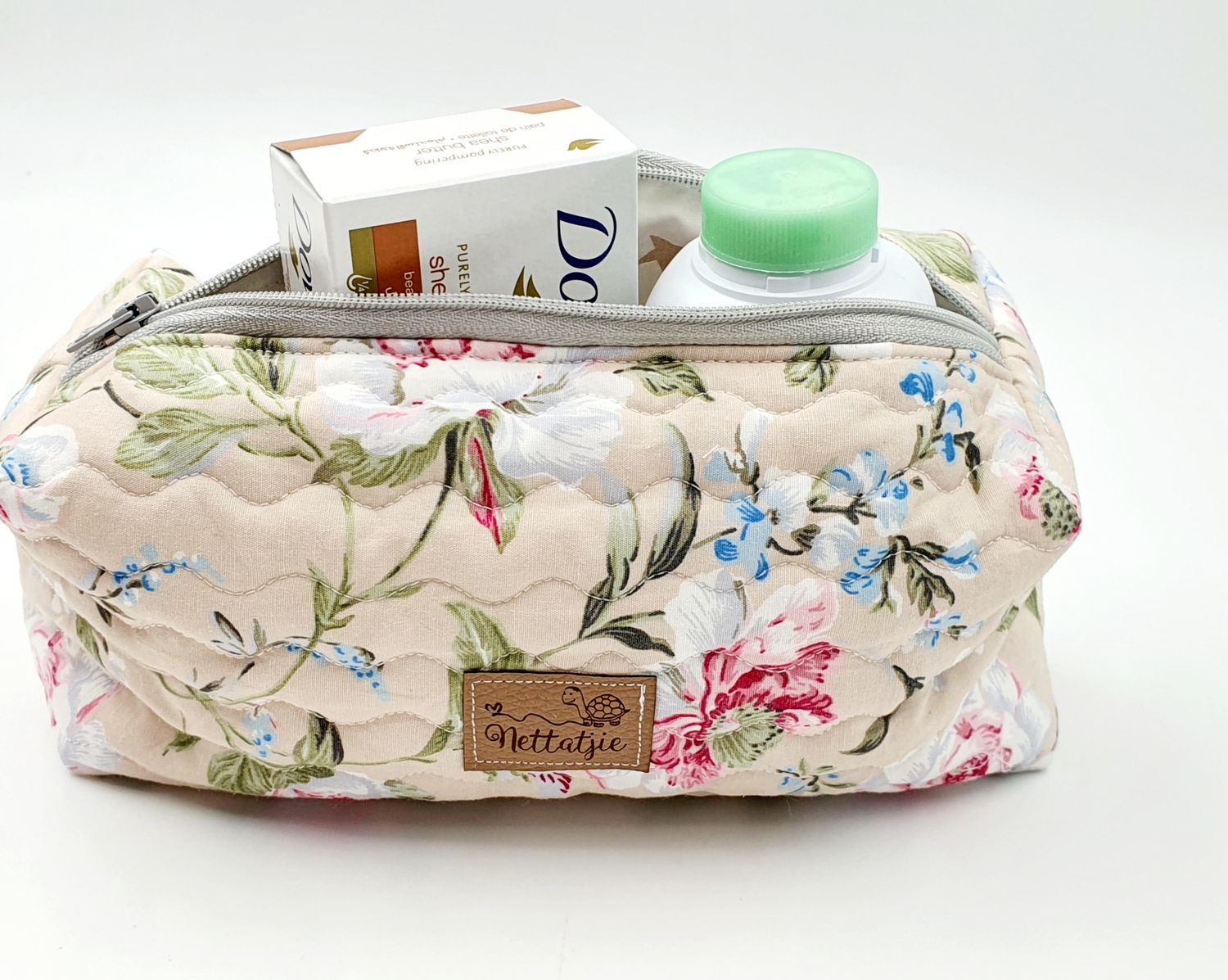 Cream colored floral print toiletry bag containing Dove soap and personal care products.