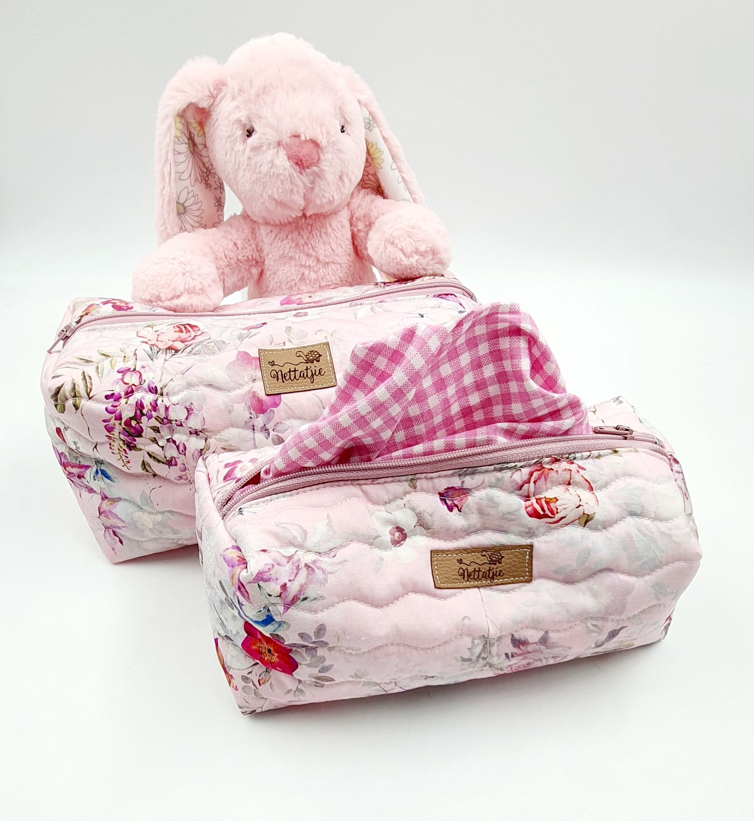 Two quilted floral toiletry bags with pink plush bunny toy on top.
