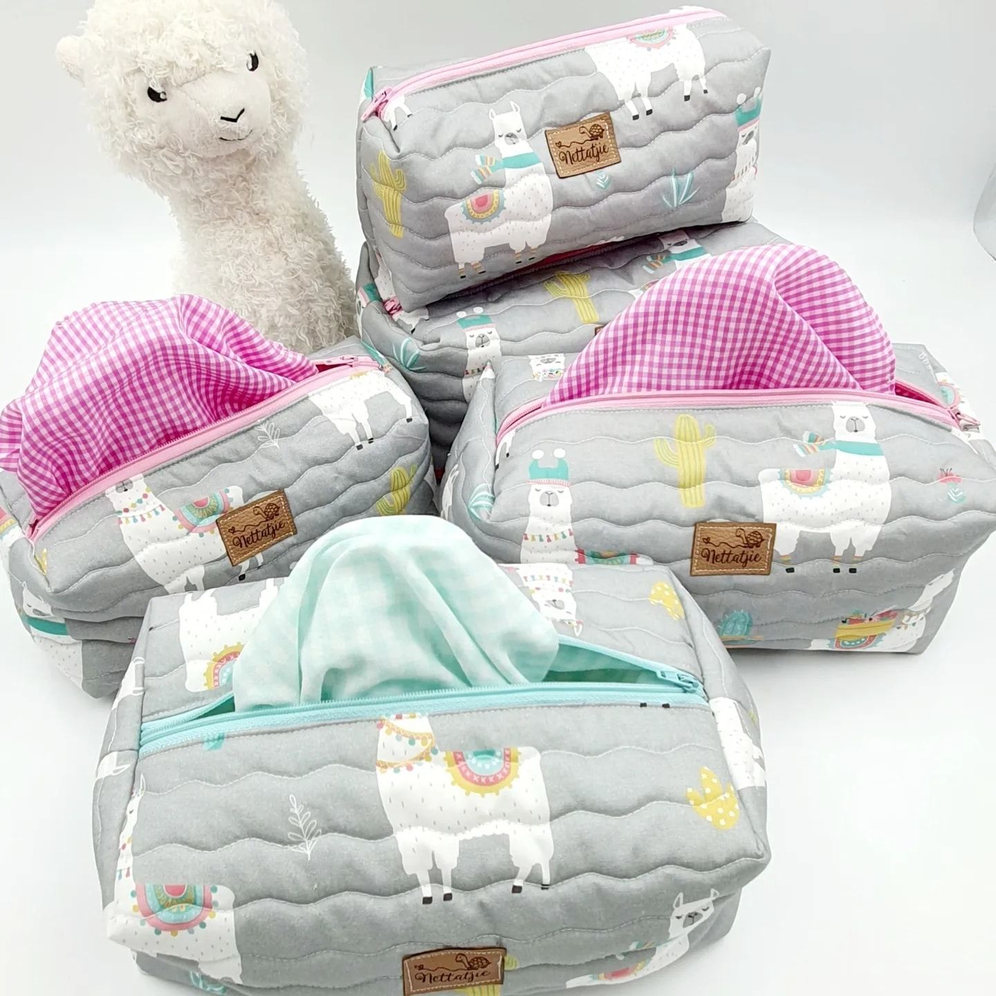 Collection of llama print diaper bags in gray with pink gingham accents.