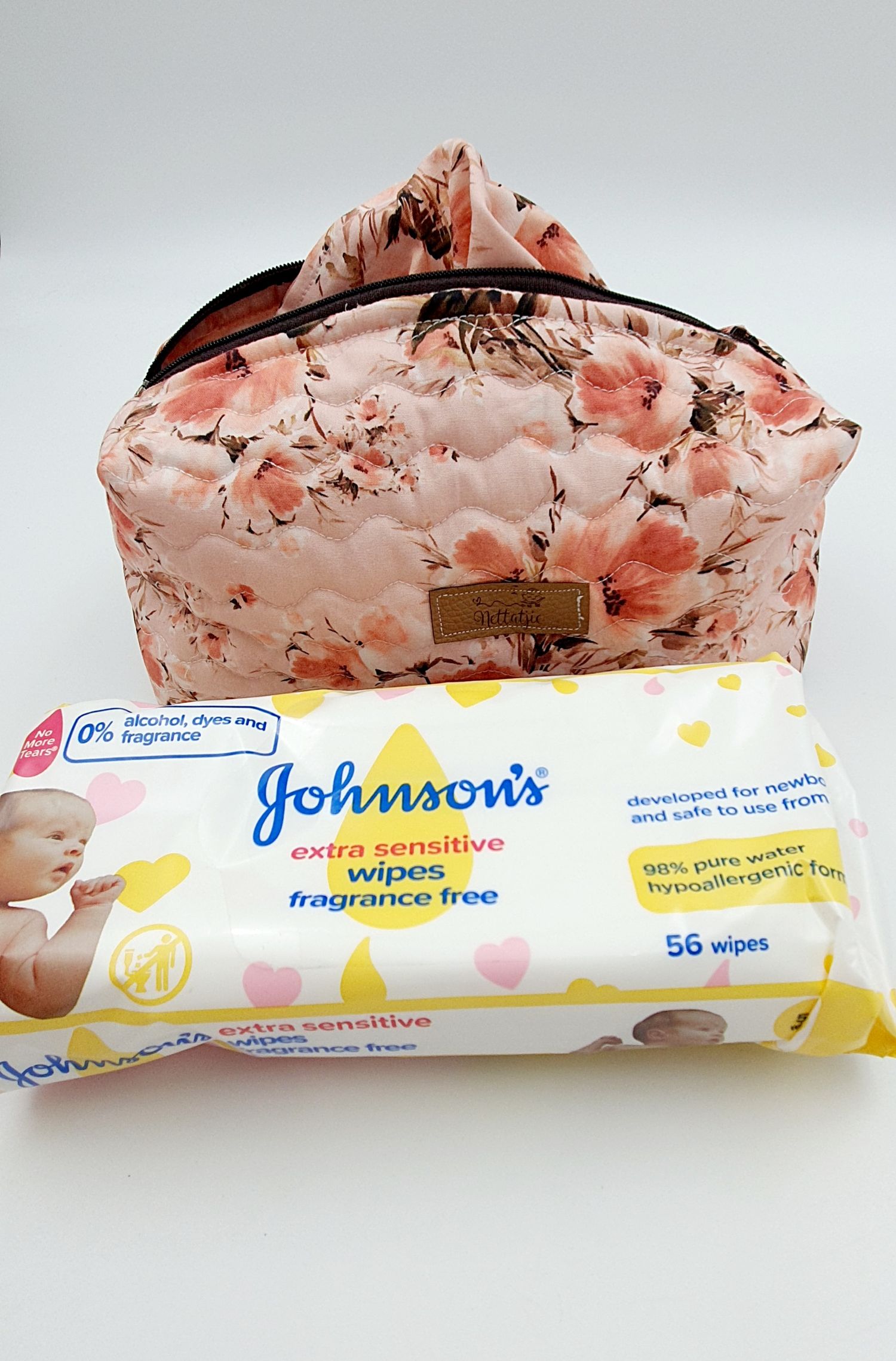 Coral floral print makeup bag with black zipper shown with Johnson's sensitive wipes package.