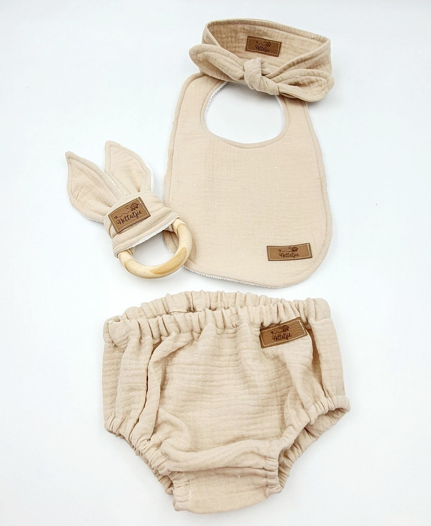 Beige organic cotton baby accessories including bib and diaper cover.