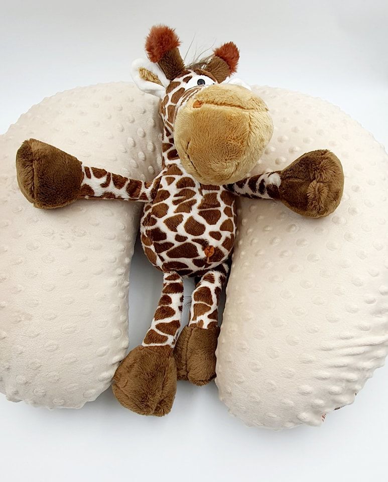 Plush giraffe stuffed animal laying on white textured surface showing spotted pattern and soft brown details.