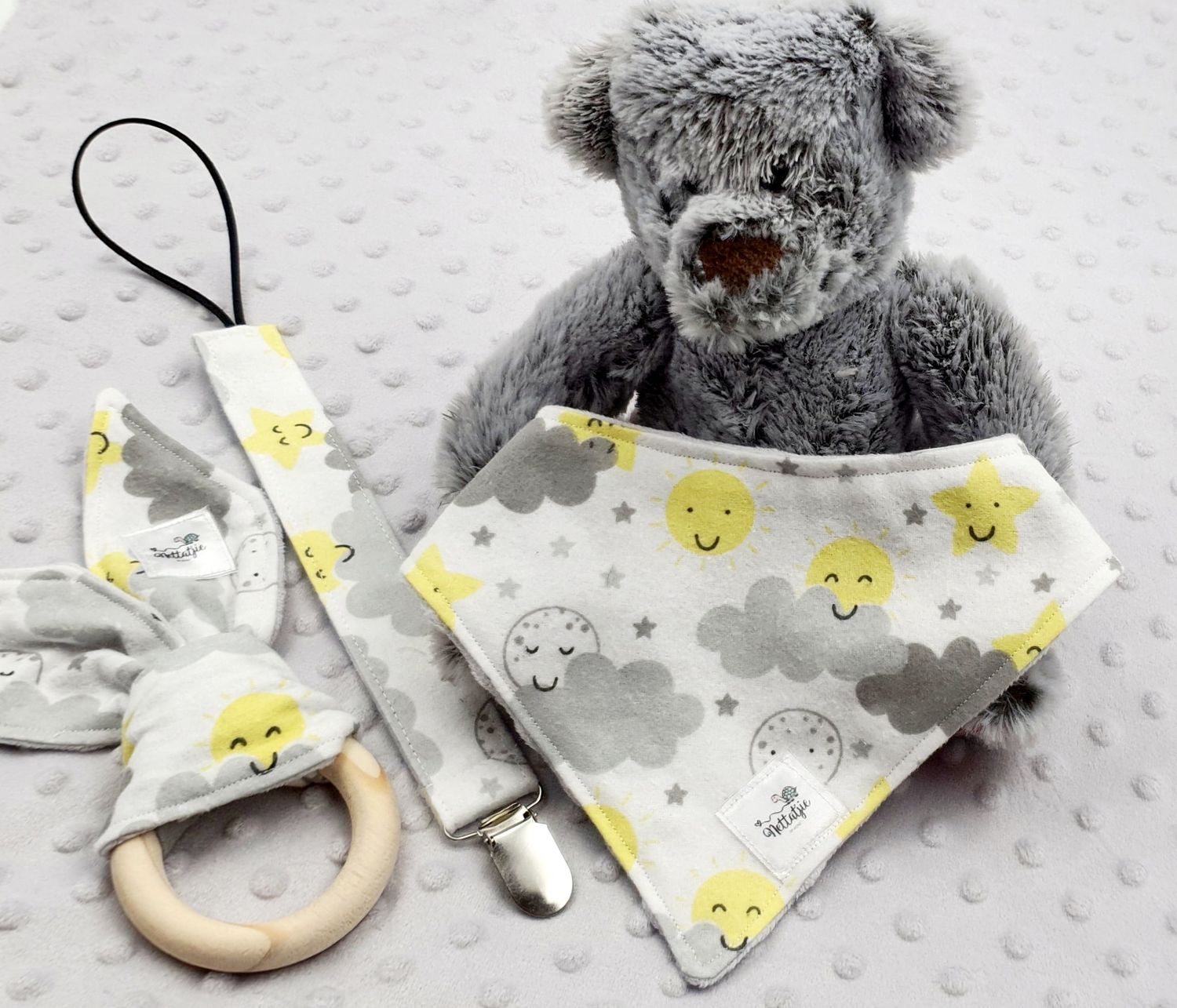 Gray teddy bear with yellow smiley face bandana and wooden teething ring.