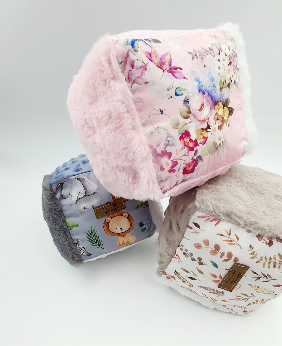 Soft pink and gray baby blankets with floral prints and animal designs laid out on white background.